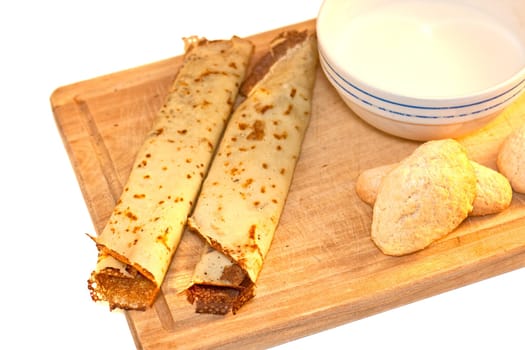 Crepes, cookies and milk on cutting board