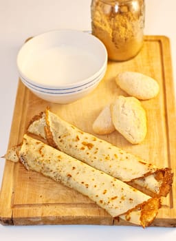Crepes, cookies and milk on cutting board