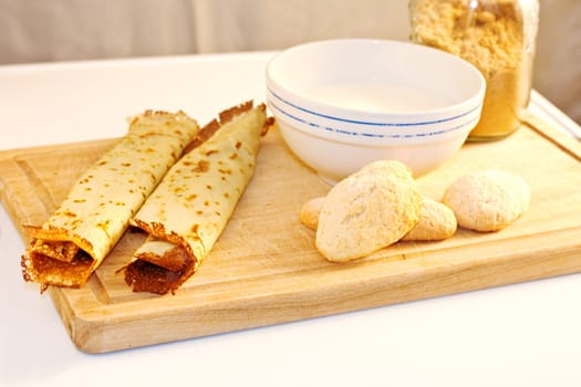 Crepes, cookies and milk on cutting board