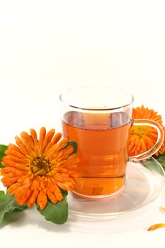 a glass of calendula tea and marigolds against a light background