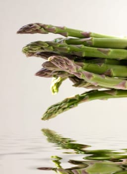 A bunch of asparagus reflected in water on a gray background
