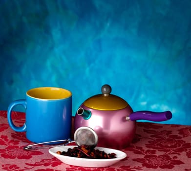 Teapot, cup and herbs on blue background