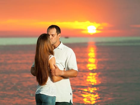 Young couple kissing near the sea at sunrise