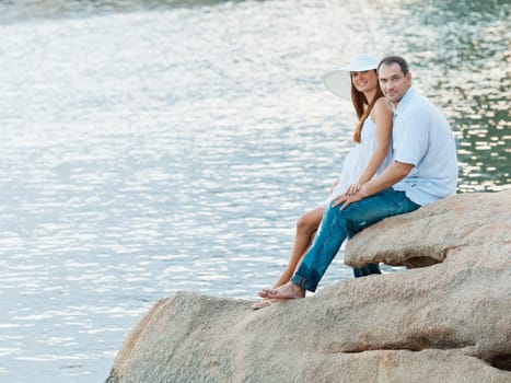 Young couple sitting on the cliff near ocean