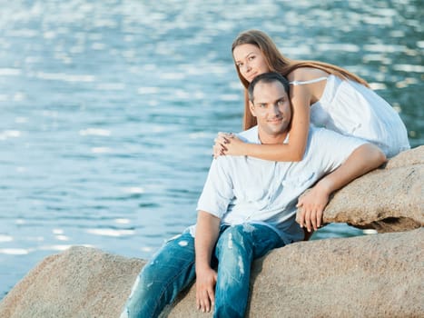 Young couple sitting on the cliff near ocean