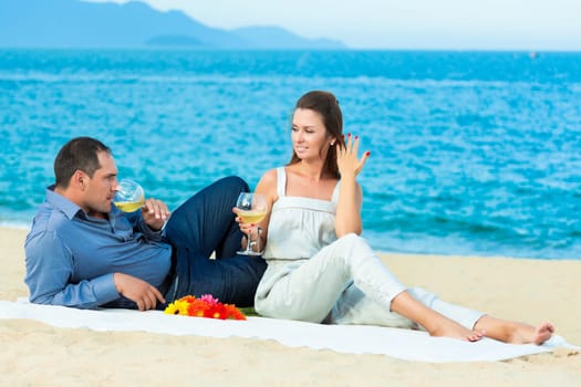 Young beautiful couple drinking wine on the beach