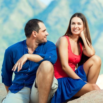 Attractive couple sitting on the cliff. Mountain on background