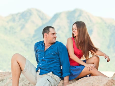 Attractive couple sitting on the cliff. Mountain on background