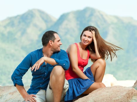 Attractive couple sitting on the cliff. Mountain on background