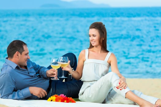 Young beautiful couple drinking wine on the beach