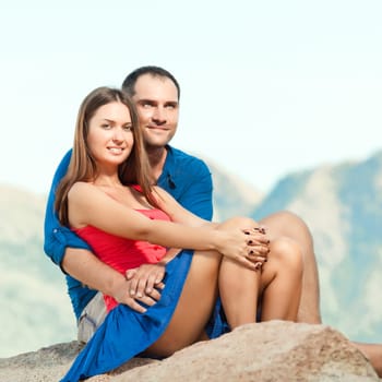 Attractive couple sitting on the cliff. Mountain on background