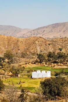 Vertical of farmland patterns of rural Rajasthan near Kumbhalgarth India with whit farm house, distant hills and blue sky