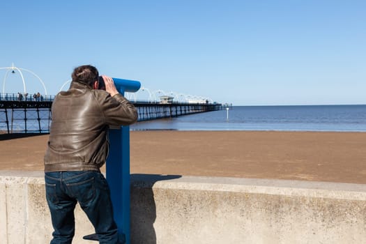 Single caucasian male looking with telescope at sea and pier in Southport England