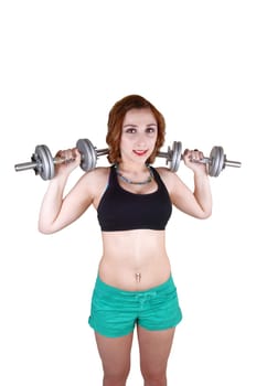 A teenage girl standing for white background in green shorts and a black sports bra, lifting up two drumbells for her exercise.