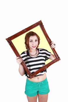 A young lovely teenage girl, standing in green shorts and a striped top in the studio holding up a picture frame, for white background.