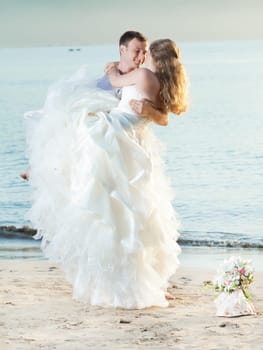 Groom holding up a his bride on the beach