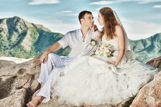 Bride and groom sitting on the rock. Mountain on background