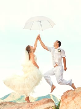 Bride and groom jumping on a rock with umbrella