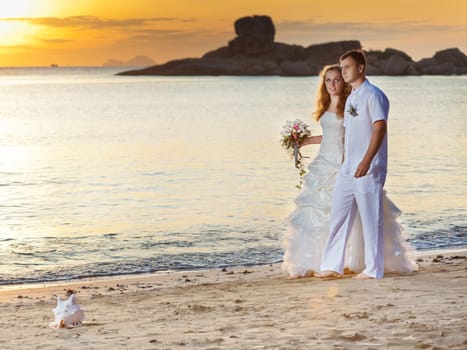 Bride and groom walking on the beach at sunrise