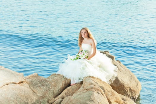 Beautiful bride sitting on a rock in a sea
