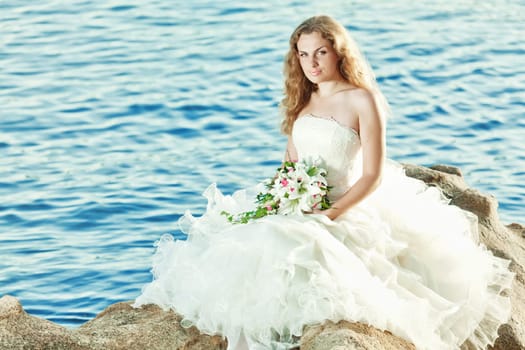 Beautiful bride sitting on a rock in a sea