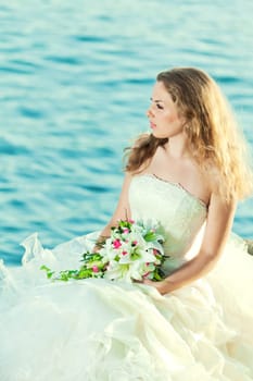 Beautiful bride sitting on a rock in a sea