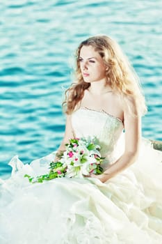 Beautiful bride sitting on a rock in a sea