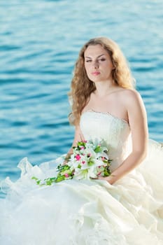 Beautiful bride sitting on a rock in a sea