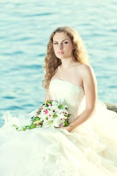 Beautiful bride sitting on a rock in a sea