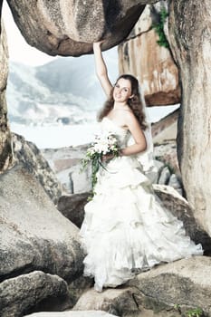 Beautiful bride holding a rock near sea