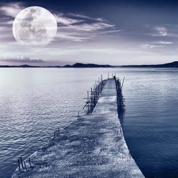 Pier on the sea at night time. Moon in the sky