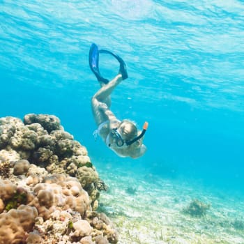 Beautiful woman diver swimming among the coral reef