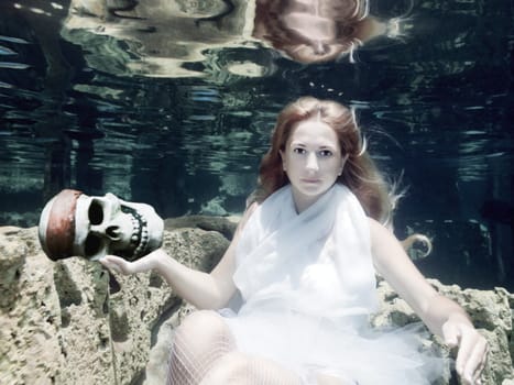 Woman with skull in white dress underwater