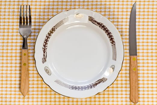 Empty dinner plate with fork and knife on tablecloth