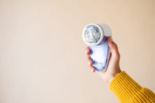 Device for shaving pellets clothes. Anti-Plush fabric Shaver. Electric portable sweater pill defuzzer. hand holding device and beige background