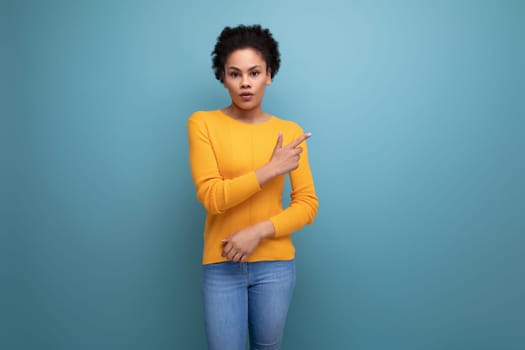 pretty 20s latin woman with afro hair in a casual yellow blouse shows her hand to the side.