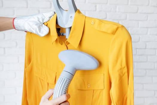 female hand using vertical steamer steaming yellow shirt. steam for ironing clothes. household appliances for the home.