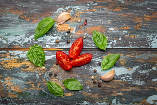 Food cooking border with cherry tomatoes, fresh green basil and garlic cloves top view on rustic colourful wooden background, ingredients for preparing meal, copy space.