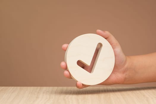 Hand holding check mark icon, banner with wooden check mark icon in hand, right sign. On a brown background. Copy space. Place for text. High quality photo