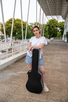 young woman from the front holding a guitar case, street music