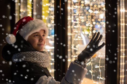 Boy in Santas hat looking and dreaming in illuminated shop window. Xmas presents holidays, or shopping on New Year or Christmas concept