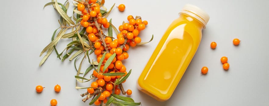 Sea buckthorn healthy juicy drink in bottle and branches with leaves and ripe berries top view on light grey simple background..