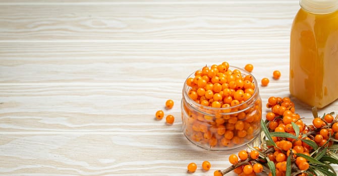 Sea buckthorn healthy drink in bottle, ripe berries in glass jar and branches with leaves top view on white wooden rustic background, great for skin, heart, vessels and immune system. Copy space..