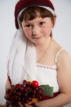 Portrait of Little girl in a stylized Tatar national costume with berries and a brush of grapes on a white background in the studio. Photo shoot of funny young teenager who is not a professional model