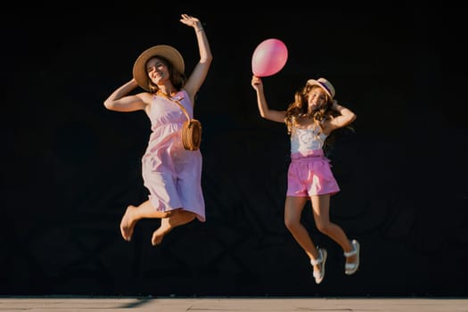 mother and daughter jumping in pink dresses with loose long hair on a black background. Enjoy communicating with each other.