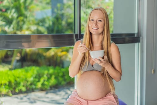 An expecting mother gracefully has breakfast on a fitness ball, illustrating the comfort it provides during pregnancy when traditional chairs may be less accommodating.