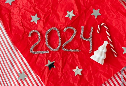 The inscription for the New Year 2024 on a red background along with a ceramic Christmas tree and a candy cane