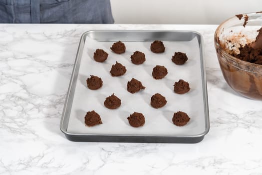 Scooping cookie dough with dough scoop into a baking sheet lined with parchment paper to bake chocolate cookies with chocolate hearts for Valentine's Day.