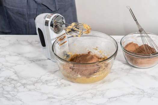 Mixing ingredients with a hand mixer to bake chocolate cookies with chocolate hearts for Valentine's Day.