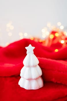 Christmas home interior with a white ceramic Christmas tree on a red blanket. Christmas and New Year concept. Vertical photo